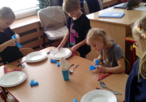 Dzieci podczas próby nakrywania do stołu i wykonania dekoracji z serwetek.